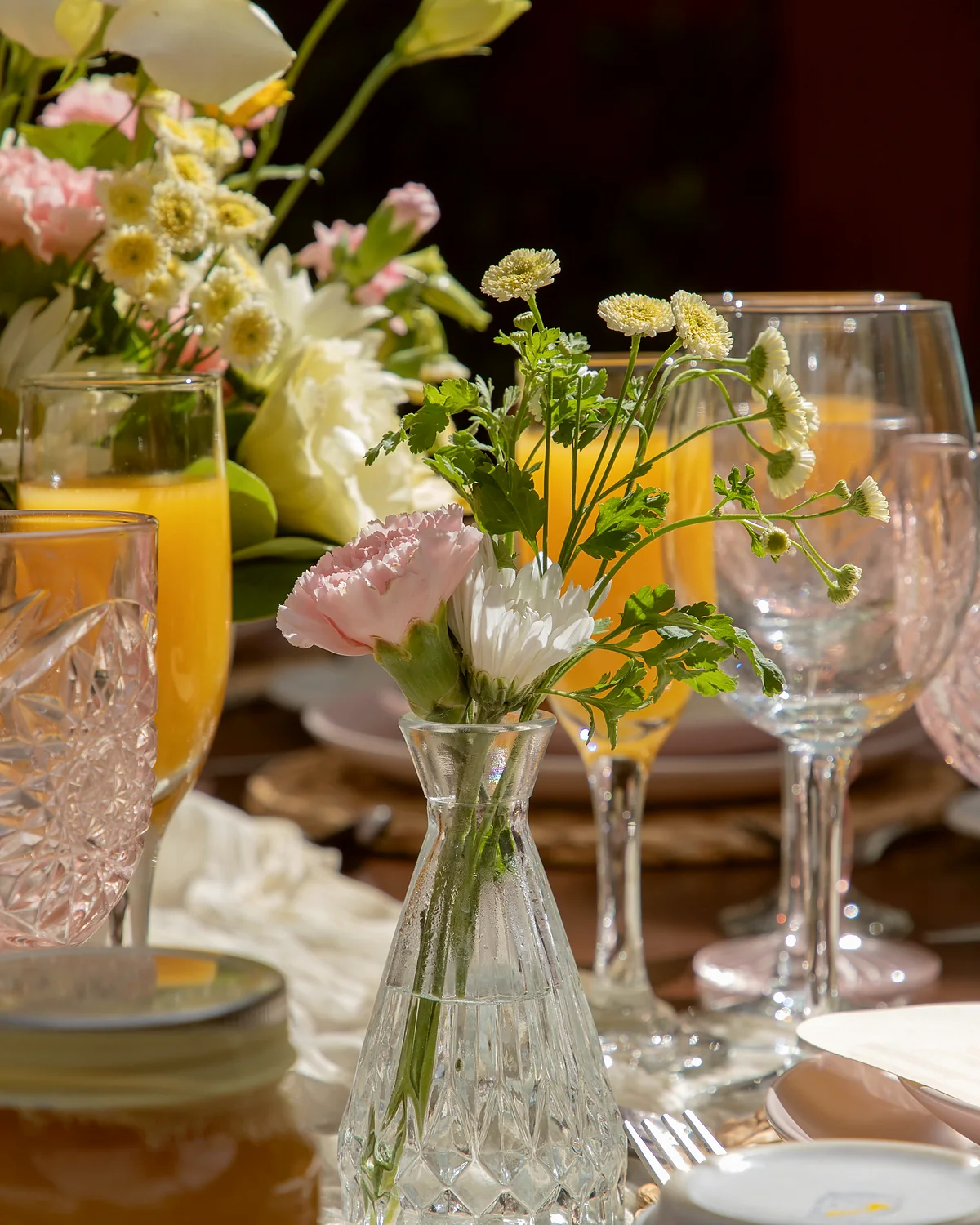 Detalle de la mesa: cristalería, jugo y arreglos de flores de temporada