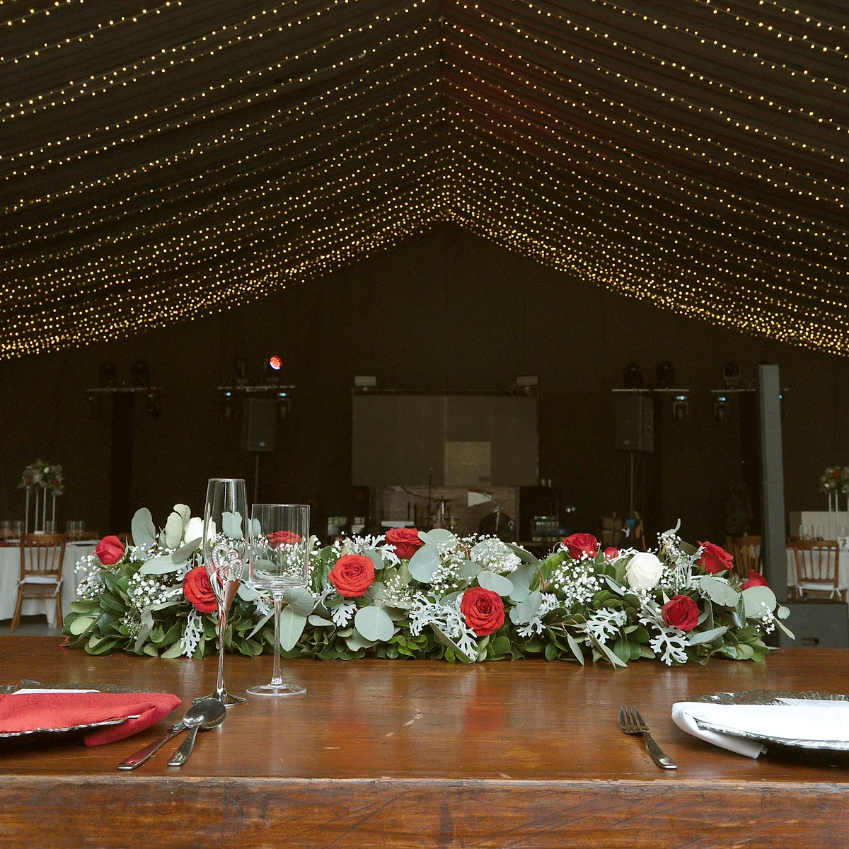 Mesa imperial con flores rojas y blancas bajo el plafón de luces