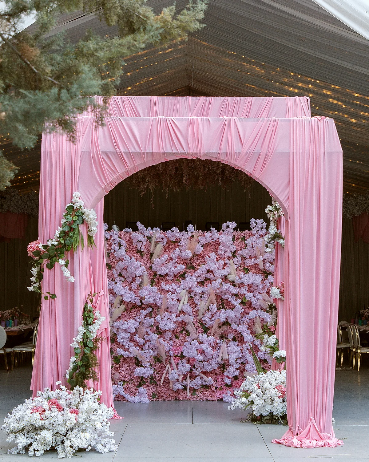 Arco drapeado en rosa con muro de flores, a la entrada de la fiesta
